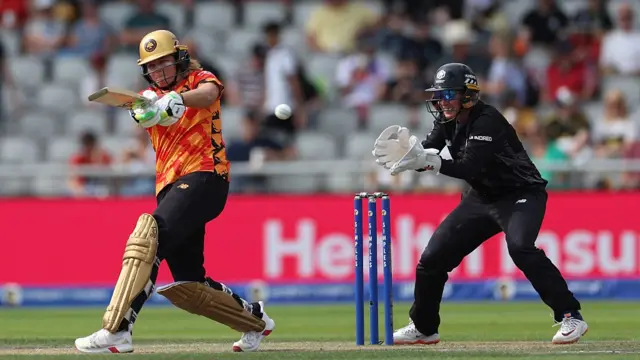 Ellyse Perry of Birmingham Phoenix bats as wicketkeeper Beth Mooney of Manchester Originals looks on