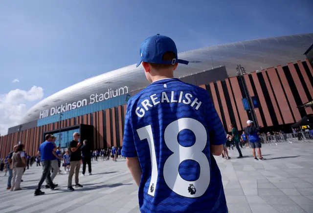A young fan with a grealish top stands looking at the new Everton stadium