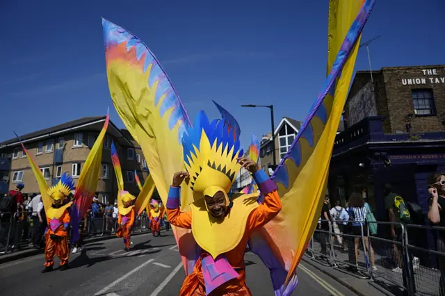 A woman in a yellow, blue and orange outfit dancing at Notting Hill Carnival.