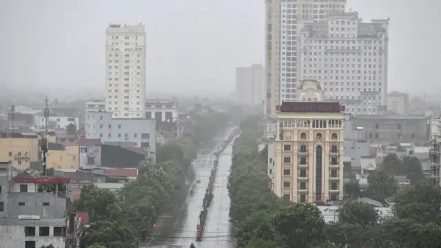 A landscape image taken from above. A two-way road is at the centre of the image with buildings either side. The sky is grey