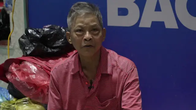 Headshot of Le Manh Tung at the centre. Plastic bags are piled up behind him