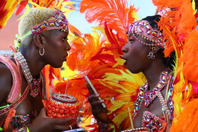 Two women in red, orange and yellow carnival outfits. Looking at each other and smiling.