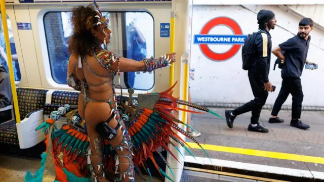 A carnival participant travels on the tube in full Carnival attire
