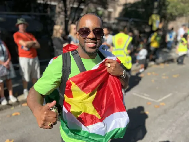 A man holds the Suriname flag while posing with his thumbs up