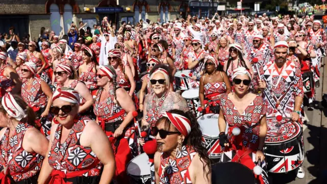 Revelers wearing red, white and black outfits bang the drums on the parade, wearing sunglasses