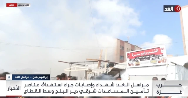 A wide shot with tents in the forground and the hospital building covered in smoke