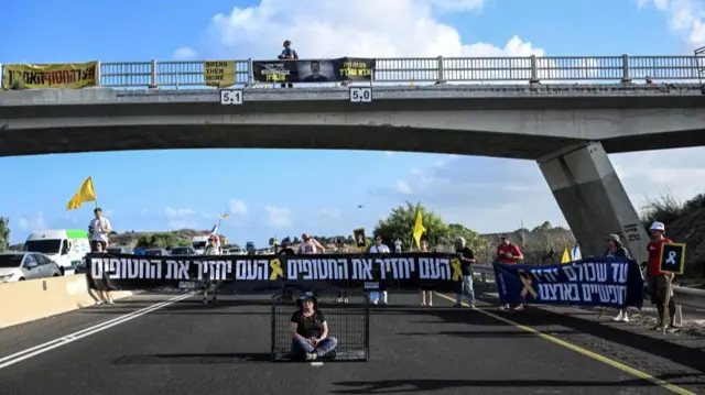 A protester sits in a cage as others hold up banners blocking the road