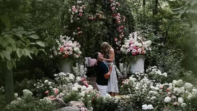 A man kneels in front of a woman, they are surrounded by flowers