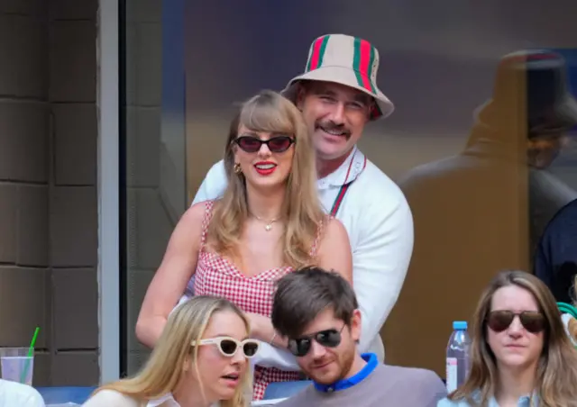 A man and a woman hold each other as they watch a tennis game.