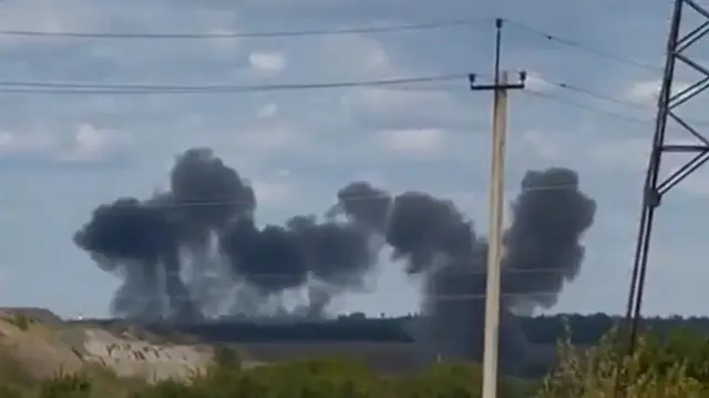 Smoke plumes in the distance with telegraph pole and a pylon in the foreground