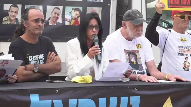 Einav Zangauker speaks at a news conference holding a microphone and is flanked either side by other protesters