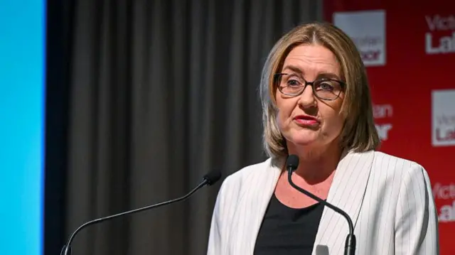 Jacinta Allan speaks into two microphones. She looks at a point beyond the camera