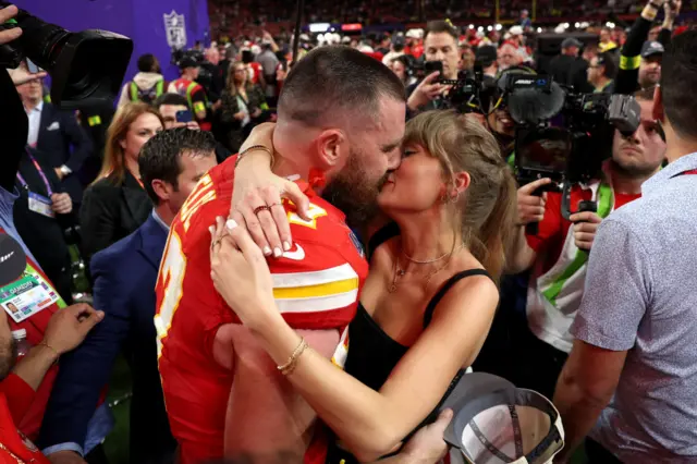 A man and a woman embrace tightly and kiss at a football game