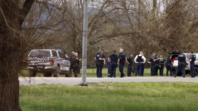 A line of police officers stand on the side of a road, near a police car