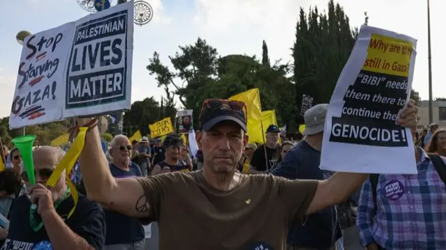 A man in Jerusalem wears a khaki tshirt and holds up two posters that say Palestinian Lives Matter