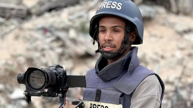Mohammed Salama wearing a hard hat and vest both reading 'PRESS' and holding a camera