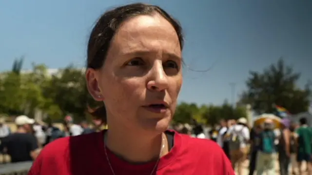 Dalia Cusnir wears a red T-shirt and looks directly at the camera. There is a blurred crowd in the background