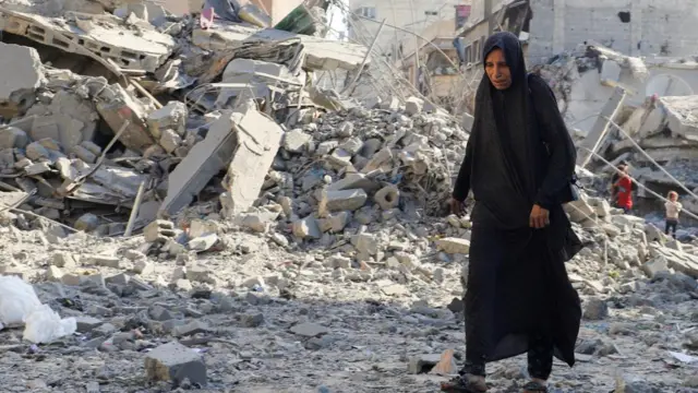 Palestinians inspect the site of an overnight Israeli strike on a house, in Gaza City. There is a mass of rubble seen in the background, and the woman in the foreground wears all baclk
