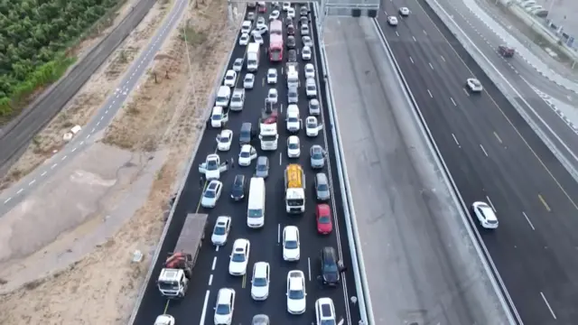 Cars are seen on a major highway, in bumper-to-bumper traffic. It does not appear to be moving