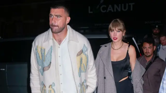 Travis Kelce and Taylor Swift exiting a car at an event, there are three people stood in a line behind them.