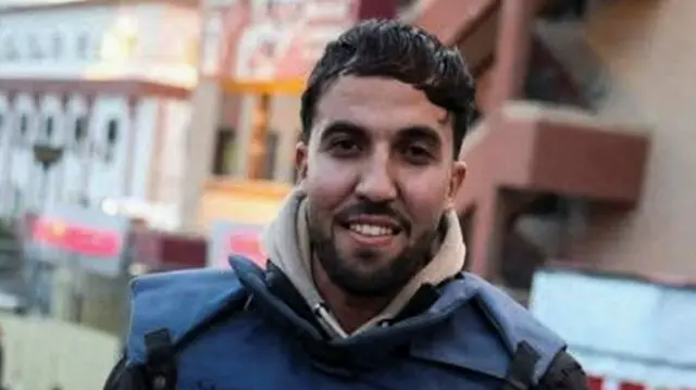 Palestinian journalist Moaz Abu Taha, a freelance journalist who worked with several news organisations including occasionally contributing to Reuters and who was killed in Israeli strikes on Nasser hospital (Moaz Abu Taha, a man standing and wearing a blue jacket with the words PRESS in capital letters on the front, looking at the camera, holding a phone in his left hand)