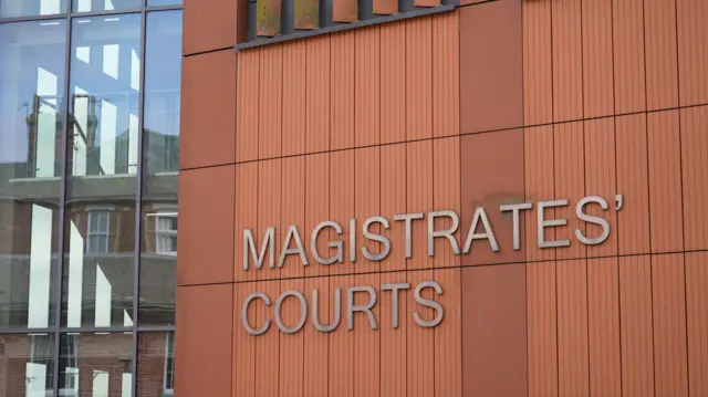A landscape image of Colchester Magistrates' Court - a red exterior with a sign reading 'Magistrates' Courts'
