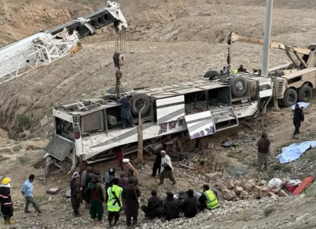 A bus overturned and two vehicles with cranes preparing to lift it