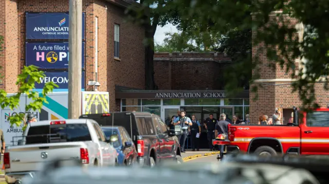 A brown brick building with cars parked in front and a sign saying 'Anunciation'
