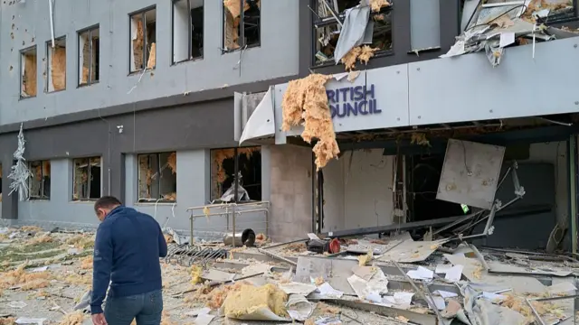 A man in a blue top and jeans walks in front of a heavily damaged building in Kyiv housing the British Council. Debris, pieces of windows and insulation are strewn to the ground