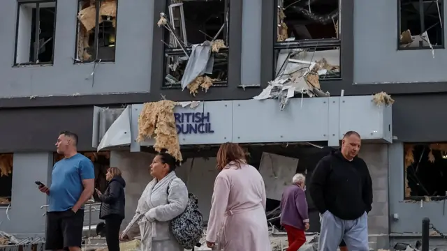 Six people (three men and three women) stand outside a heavily damaged building in Kyiv. The building houses the British Council, the name displayed in blue letterings on the front