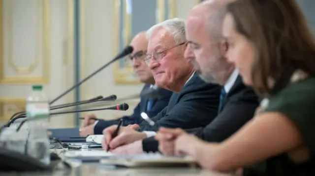 Keith Kellogg sits in a line of people along a table with microphones in front of them.