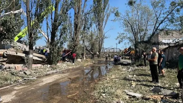 A path in Kyiv filled with water as people stand nearby looking at burning rubble.