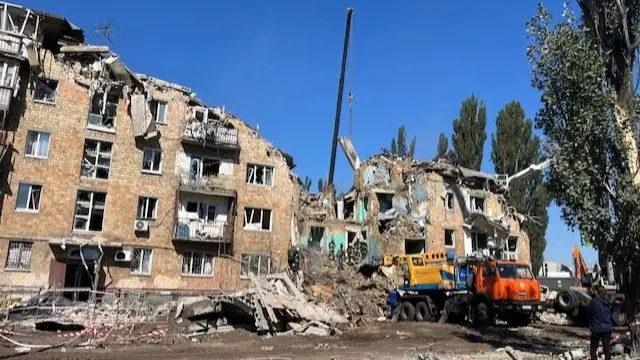 Cranes and diggers work on a partially crumbled block of flats