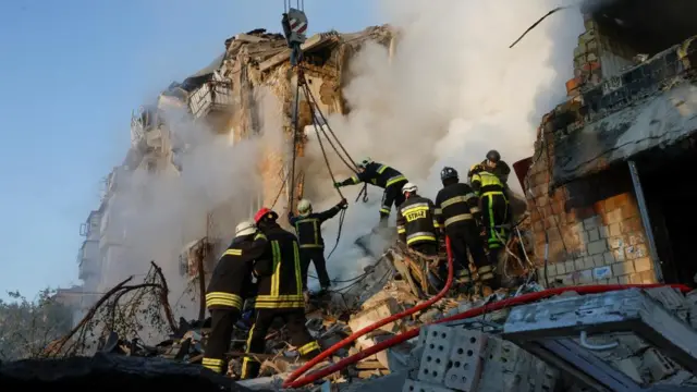 Emergency service workers in high vis outfits attend the smoking ruins of a Kyiv building