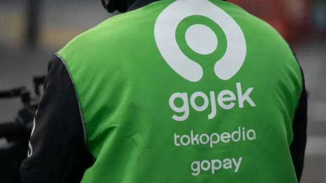 Backview of a motor rider with a bright green Gojek jacket with the company's logo