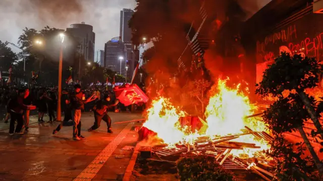 Protesters throwing objects into a fire outside the police headquarters