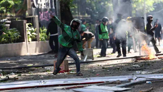 Protestor in helmet and green jacket throws an object