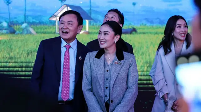 Paetongtarn and Thaksin wearing suits and smiling, looking in the same direction