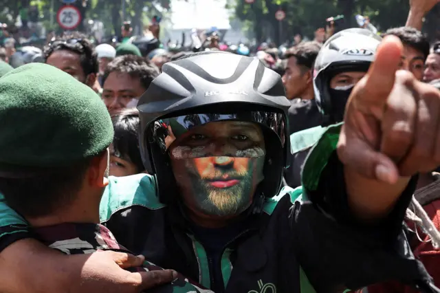 A man wearing a face mask and motorcycle helmet is restrained by police