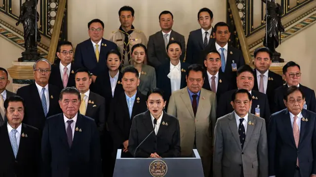 Paetongtarn stands at a lectern, speaking. Ministers and aides standing in rows on the stairs behind her.