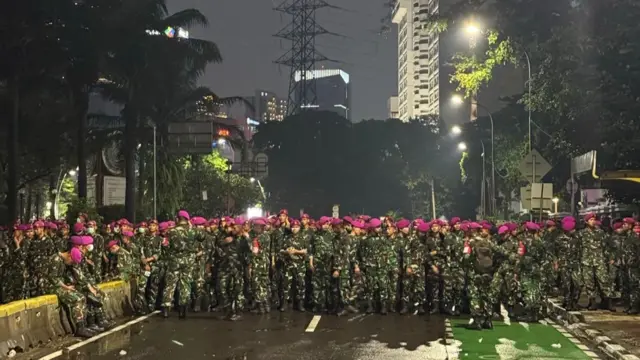 A crowd of officers in red berets and military fatigues block a city street