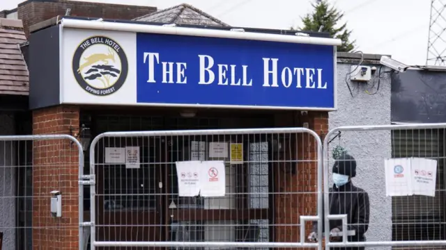 Staff member looks out from behind a gate outside The Bell Hotel in Epping, Essex