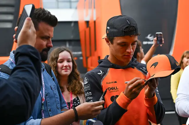 Lando Norris signs a cap for a fan