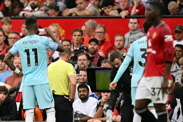 Referee Sam Barrott (C) reviews the on field monitor before awarding Manchester United a late penalty