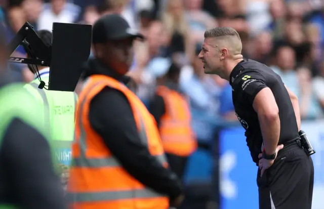 Referee Robert Jones looks at a VAR screen before disallowing a Fulham's Josh King goal