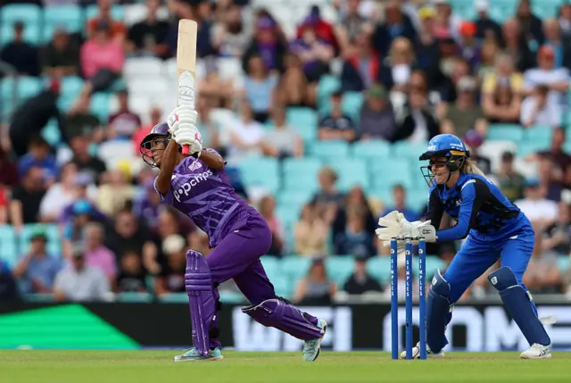 Davina Perrin of Northern Superchargers hits out as wicket keeper Georgia Redmayne of London Spirit looks on