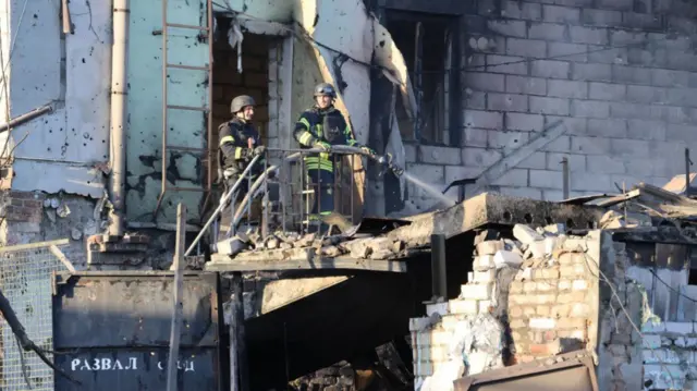 Firefighters at site of Russian strike in Ukraine, hosing water on building.