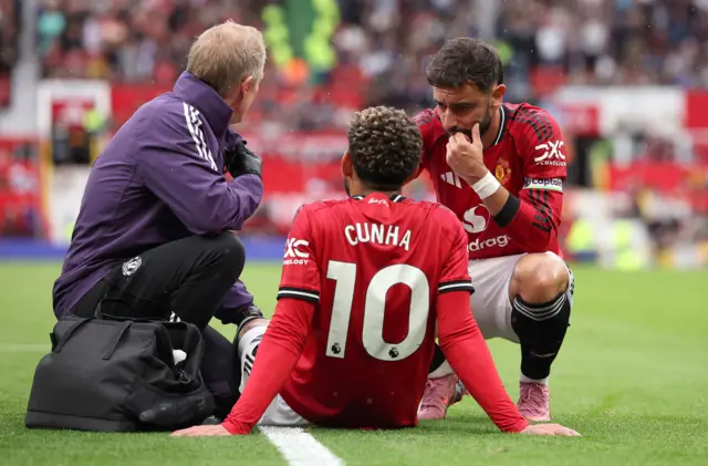 Manchester United captain Bruno Fernandes (R) speaks to teammate Matheus Cunha who receives treatment