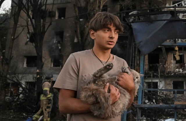 A resident holds his a cat as he stand near his apartment building, hit during a Russian drone and missile strike, amid Russia's attack on Ukraine, in Zaporizhzhia
