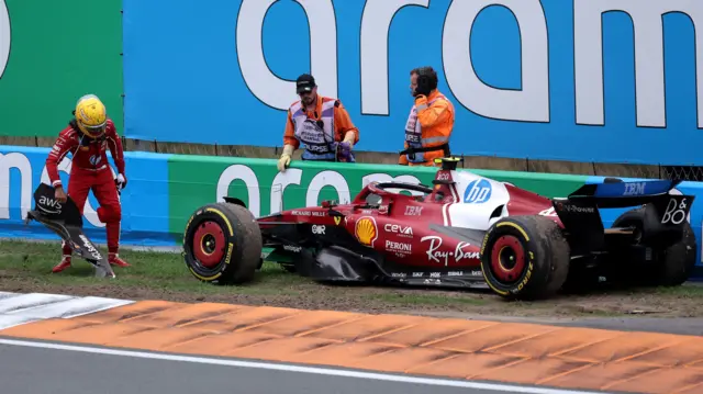 Lewis Hamilton picks up part of his front wing after crashing his Ferrari into the barrier during the Dutrch Grand Prix